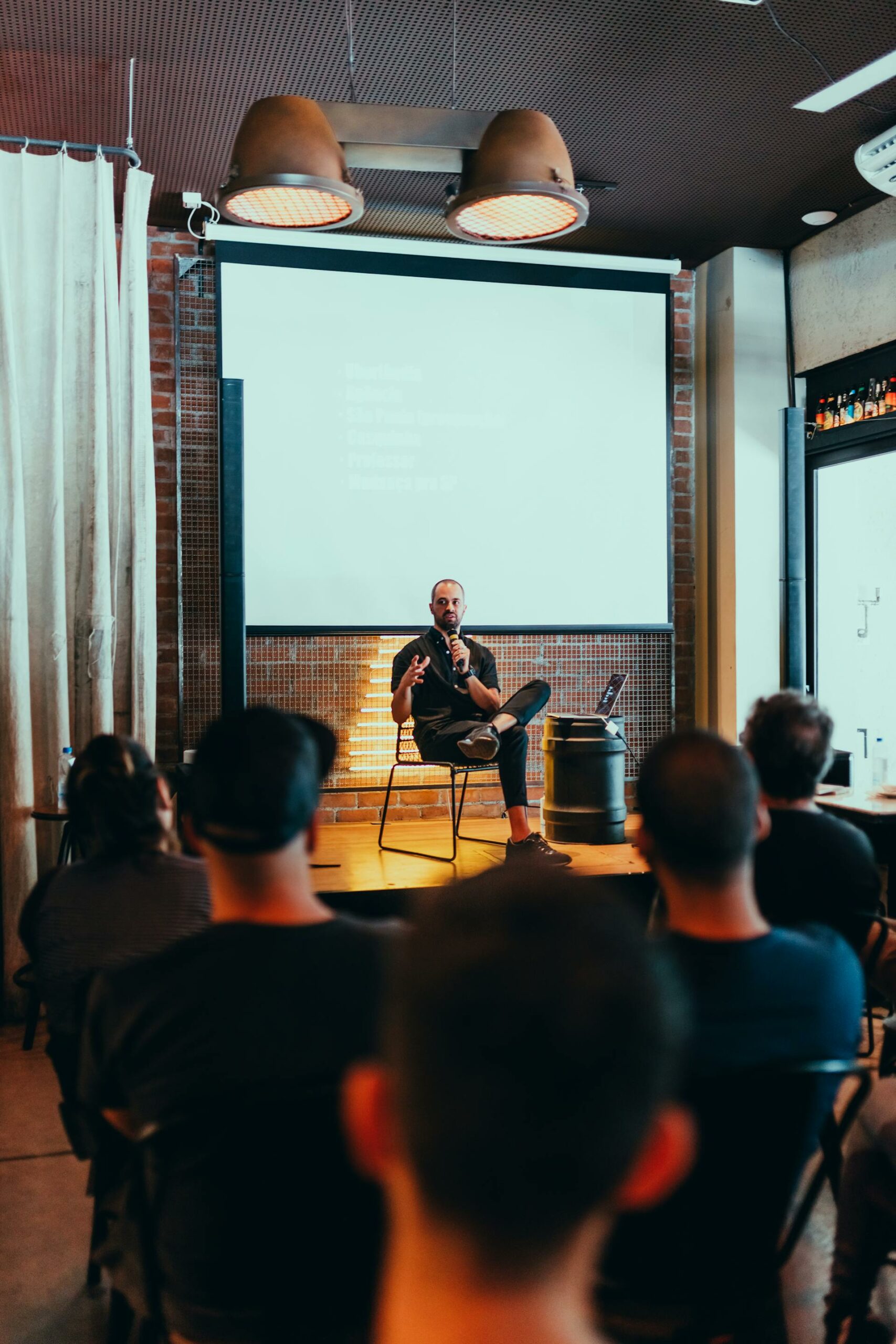 Un homme assis devant une foule lors d'une masterclass avec Fair Formations, offrant un éclairage inspirant sur un sujet, un modèle innovant de communication